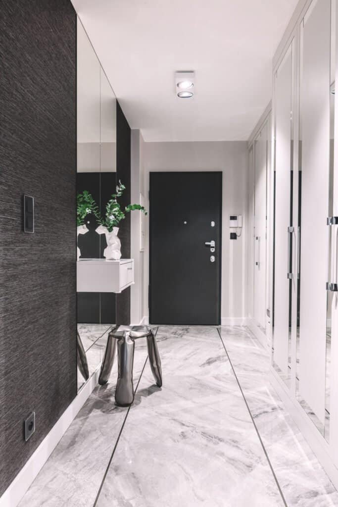 Contemporary hallway with marble tiles, black door, and white cabinetry.